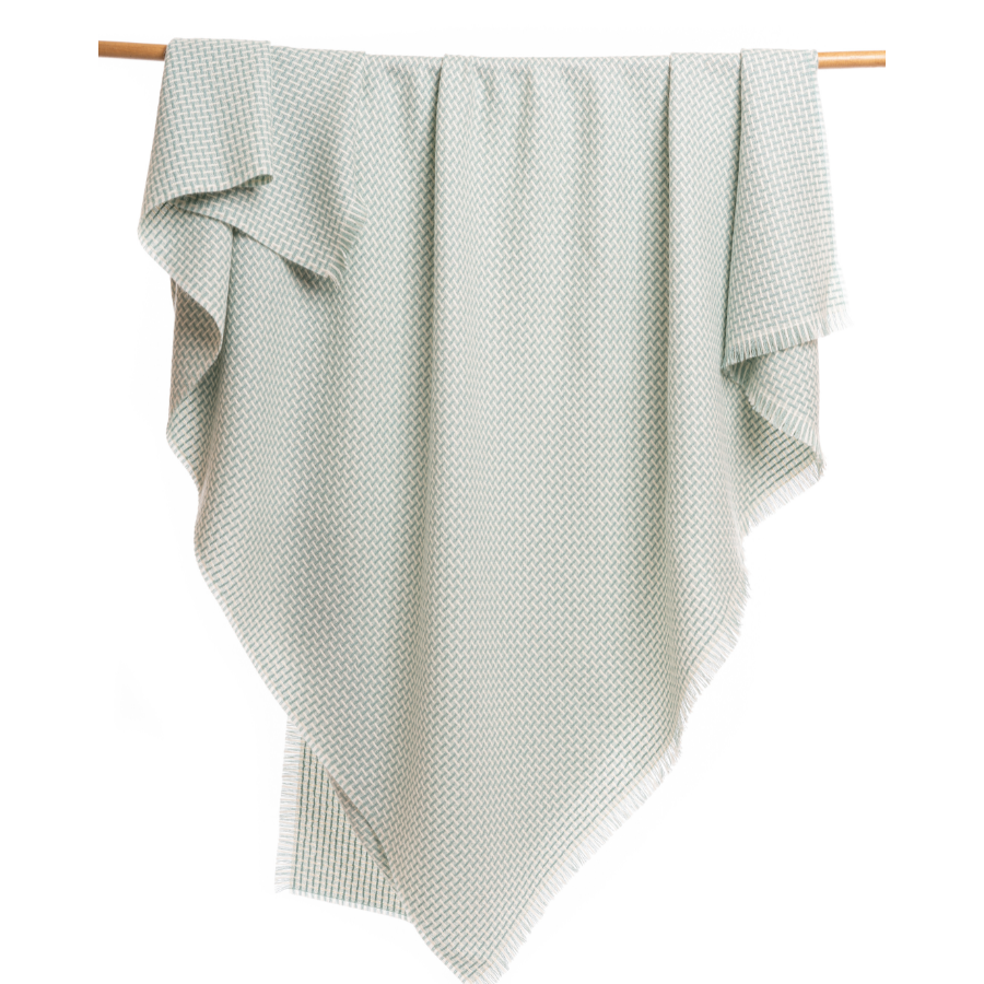 An Alpacas of Montana soft cozy luxury warm mint green and natural white woven blanket with a tasseled edge.