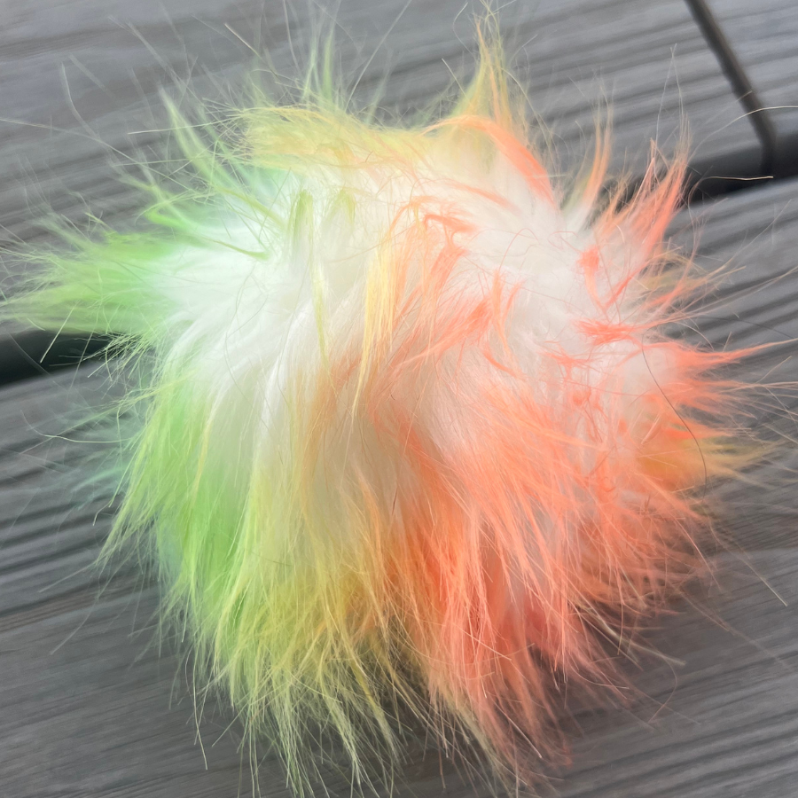A close up photo of the frosted tips pom pom, a white based pom with bright orange, yellow, and green tips on the fluff.