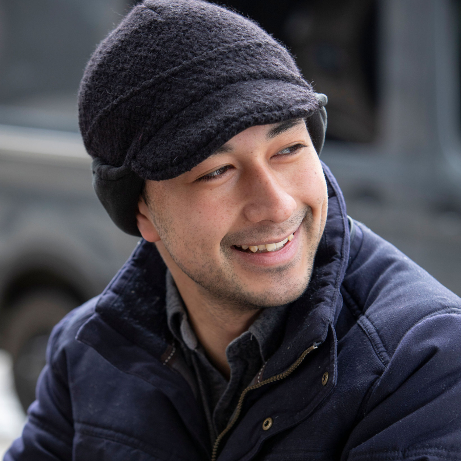 A man smiling and looking sideways wearing a black extremely warm cozy soft windproof comfortable moisture wicking thermal winter alpaca fleece wool city commuter hat.