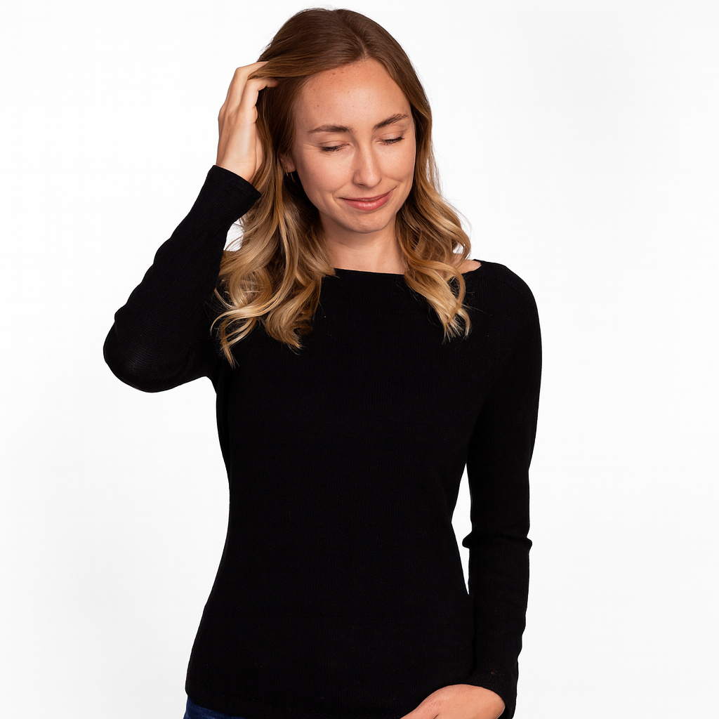 Woman wearing a fitted black baby alpaca sweater with long sleeves, gently touching her hair while smiling softly against a clean white background.