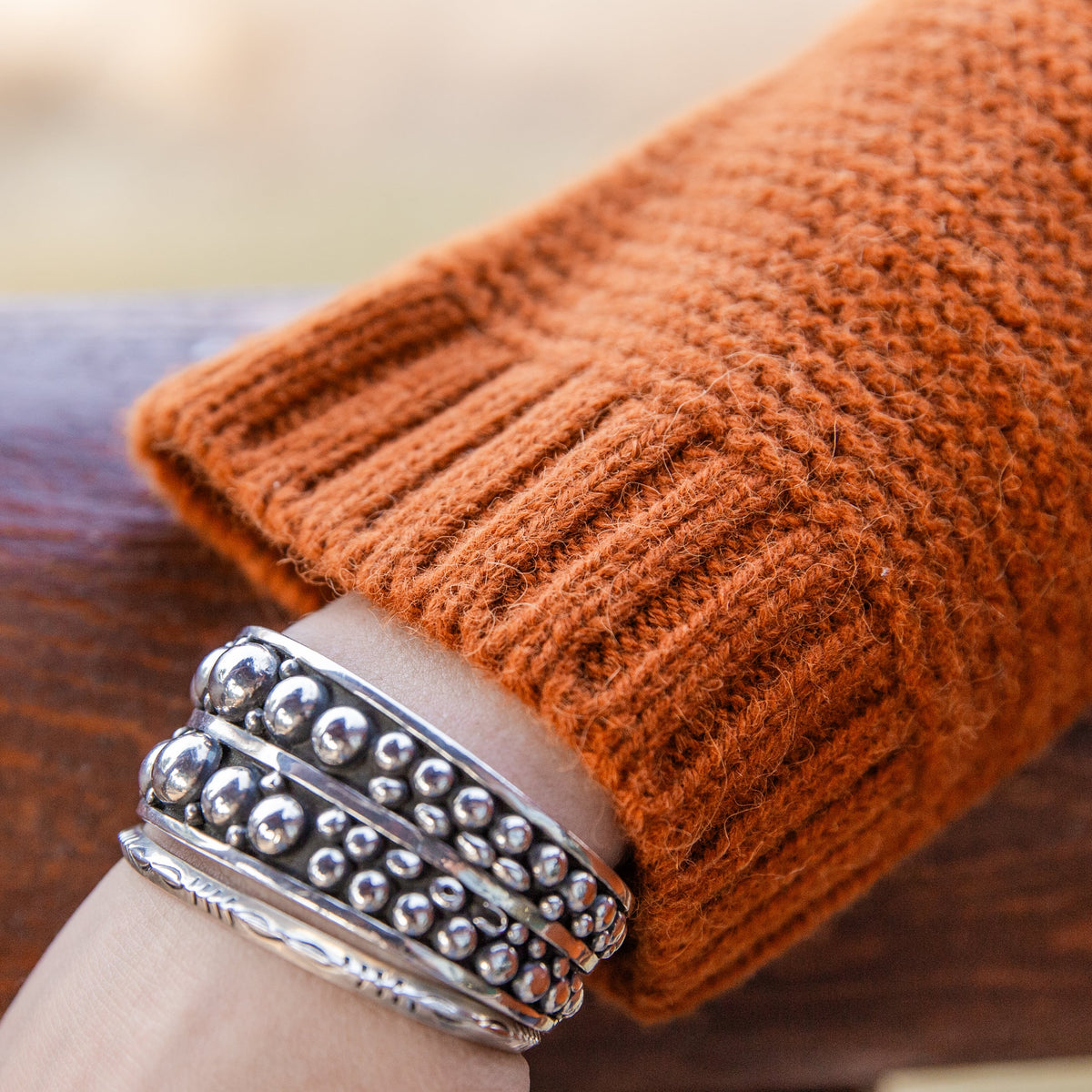 A close-up of a woman&#39;s wrist wearing silver bracelets and the soft comfortable cute fashionable cozy sweater in the color autumn orange.