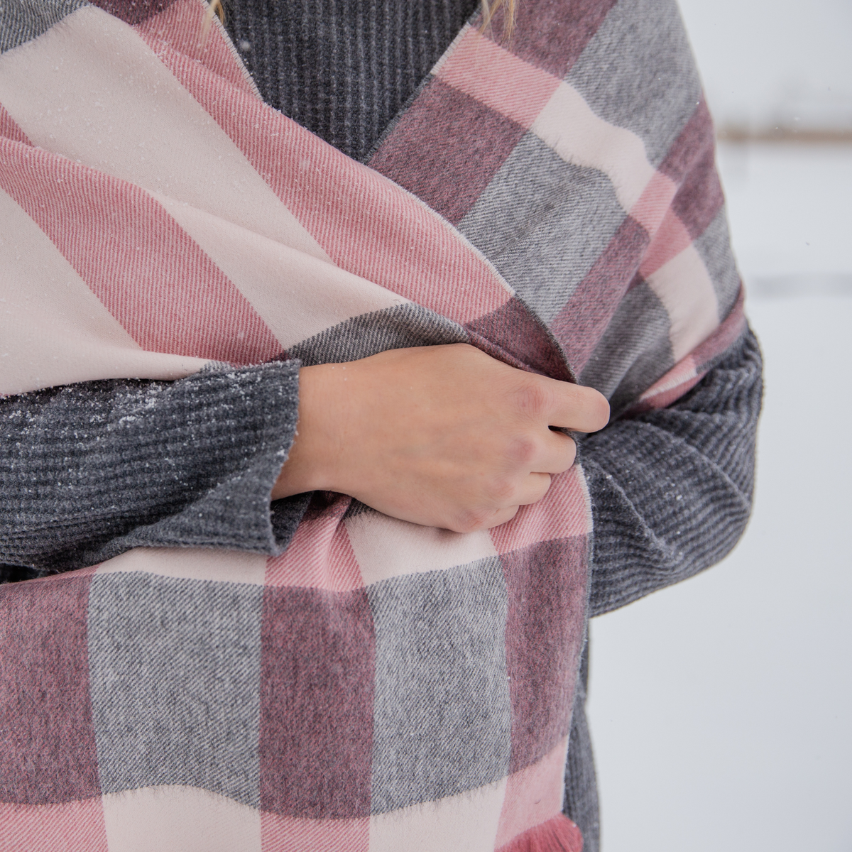 A close up photo of someone wearing a gray sweater and wrapping a scarf around them. The scarf is the beautiful soft cozy luxury stylish fashion comfortable accessory pink blush, light gray, and natural white alpaca wool scarf with tassels.