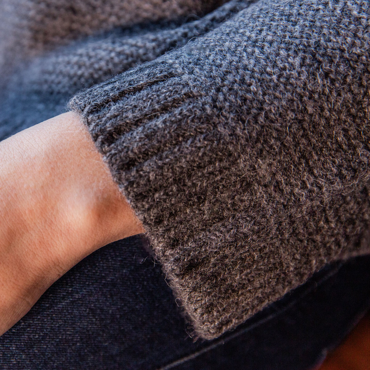 A close-up of a woman&#39;s wrist wearing the soft comfortable cute fashionable cozy sweater in the color gray.