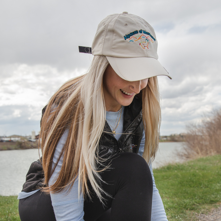 Blonde woman kneeling down towards the camera wearing a Nike and Alpacas of Montana stretch lite athletic vest and a branded logo comfortable summer breathable fashionable white baseball cap.