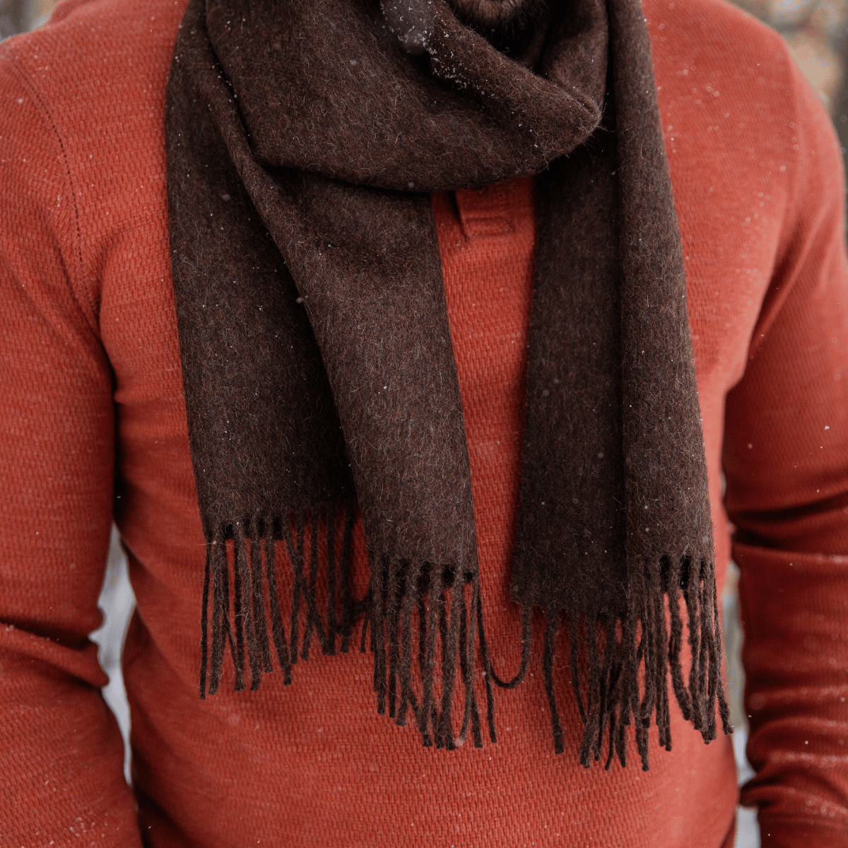 A close up of a man's chest wearing a burnt orange long sleeve shirt and an Alpacas of Montana soft stylish women's fashion comfortable cozy cute warm alpaca wool chocolate brown solid woven scarf with tassels.