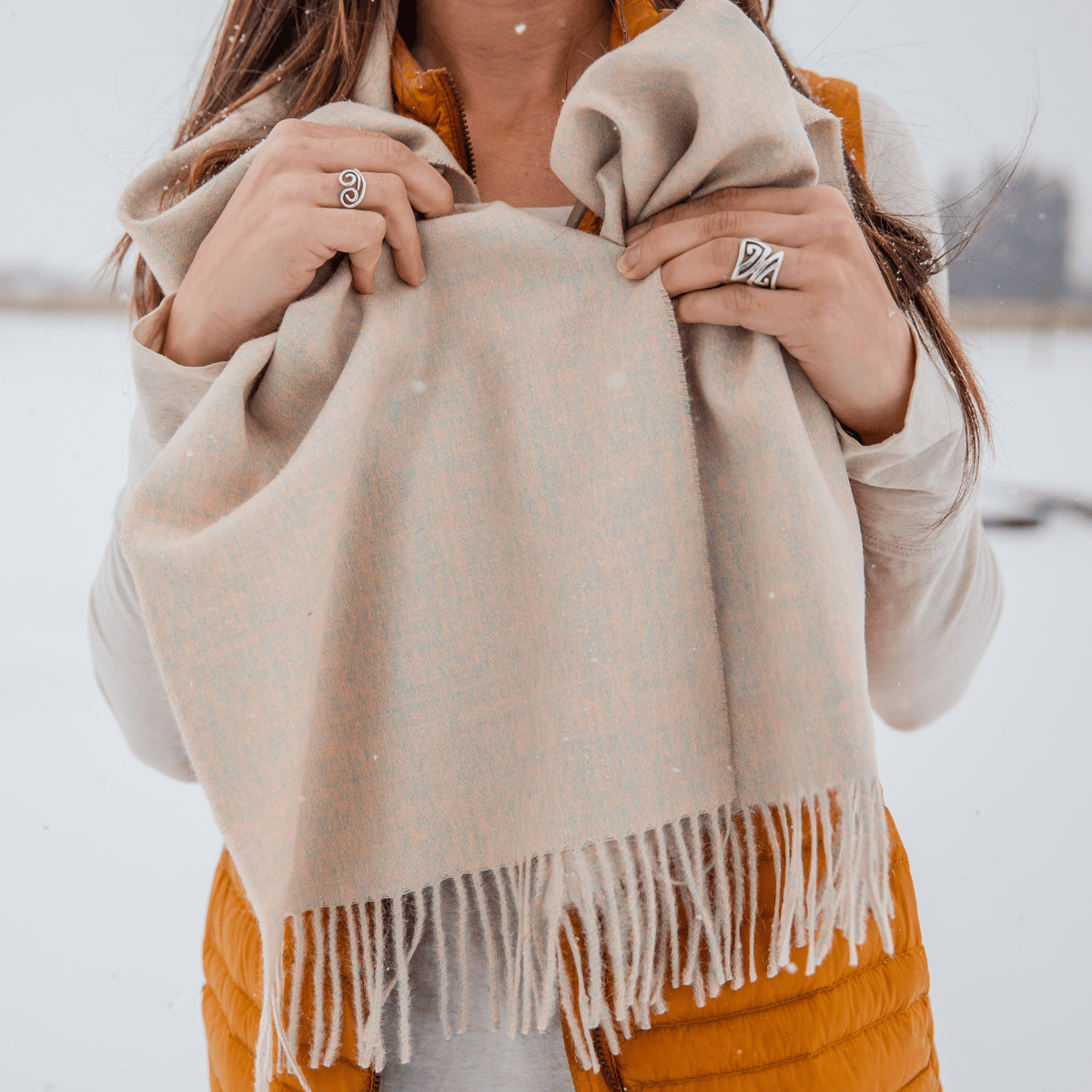 A close up photo of a woman holding an Alpacas of Montana soft stylish women&#39;s fashion comfortable cozy cute warm alpaca wool taupe color solid woven scarf with tassels.