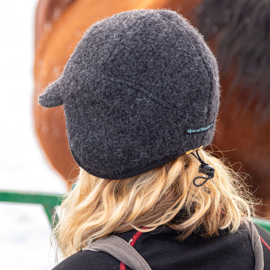 A close up of a blonde woman facing away from the camera wearing an extremely warm cozy soft windproof comfortable moisture wicking thermal alpaca fleece wool gray windstopper winter hat for hiking, skiing, hunting, fishing, outdoors.