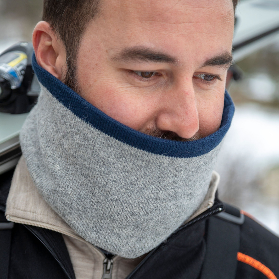 A close up of a man wearing an Alpacas of Montana lightweight cozy comfortable moisture wicking antimicrobial warm breathable all seasons thin thermal outerwear skiing hiking climbing outdoors hunting fishing rocky mountain neck gaiter made from light gray and navy blue alpaca wool.