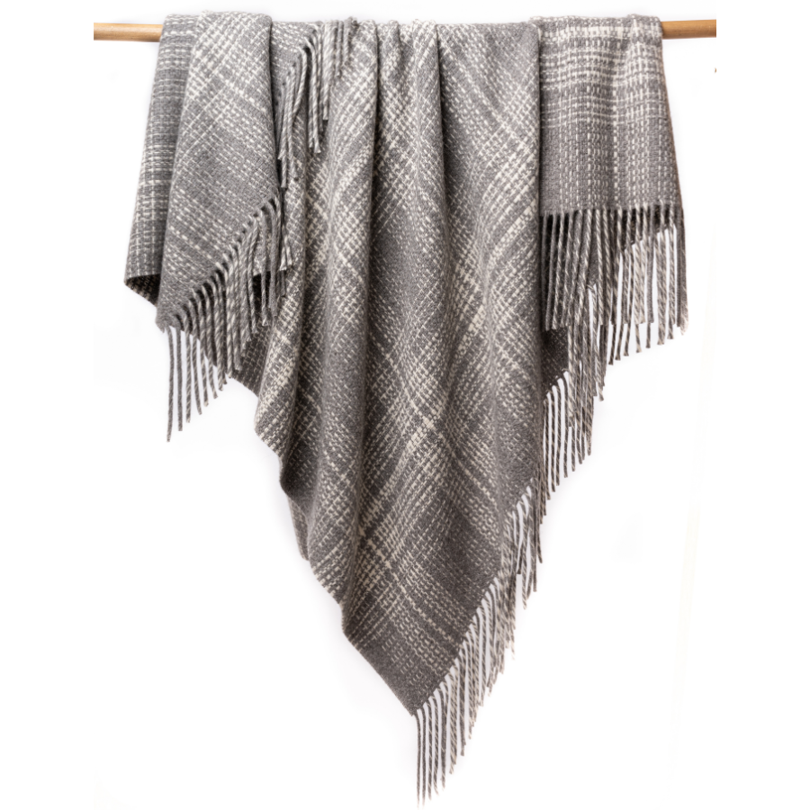 An Alpacas of Montana soft cozy luxury warm light charcoal gray with natural white accent heather plaid blanket with a tasseled edge.