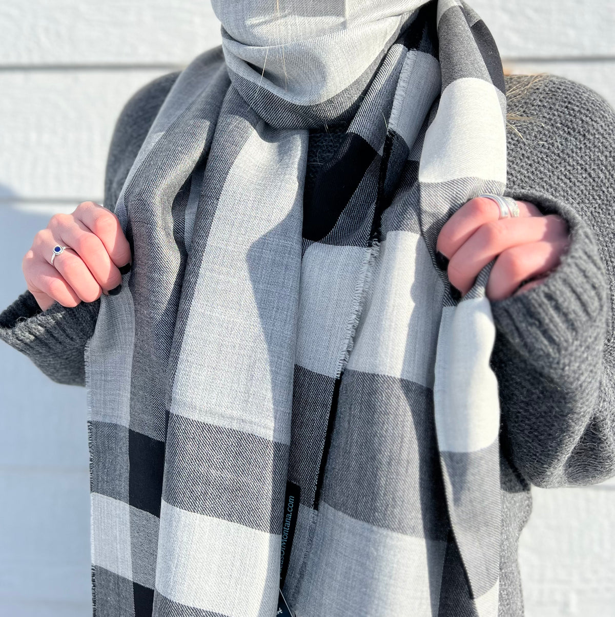 A torso-only photo of a woman wearing a charcoal gray Alpacas of Montana Cozy Knit Sweater and a soft comfortable cozy lightweight elegant fashion beautiful silk and alpaca wool woven black, charcoal, light gray, and white scarf.