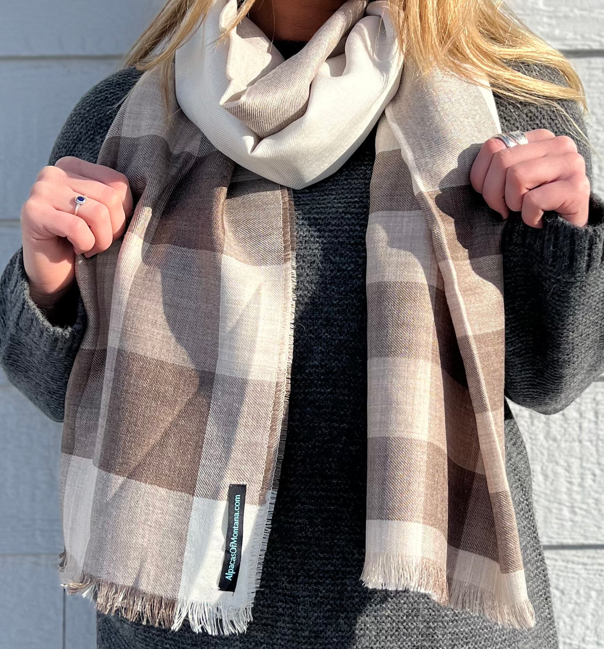 A torso-only photo of a woman wearing a charcoal gray Alpacas of Montana Cozy Knit Sweater and a soft comfortable cozy lightweight elegant fashion beautiful silk and alpaca wool woven chocolate brown, chestnut, latte, and white scarf.
