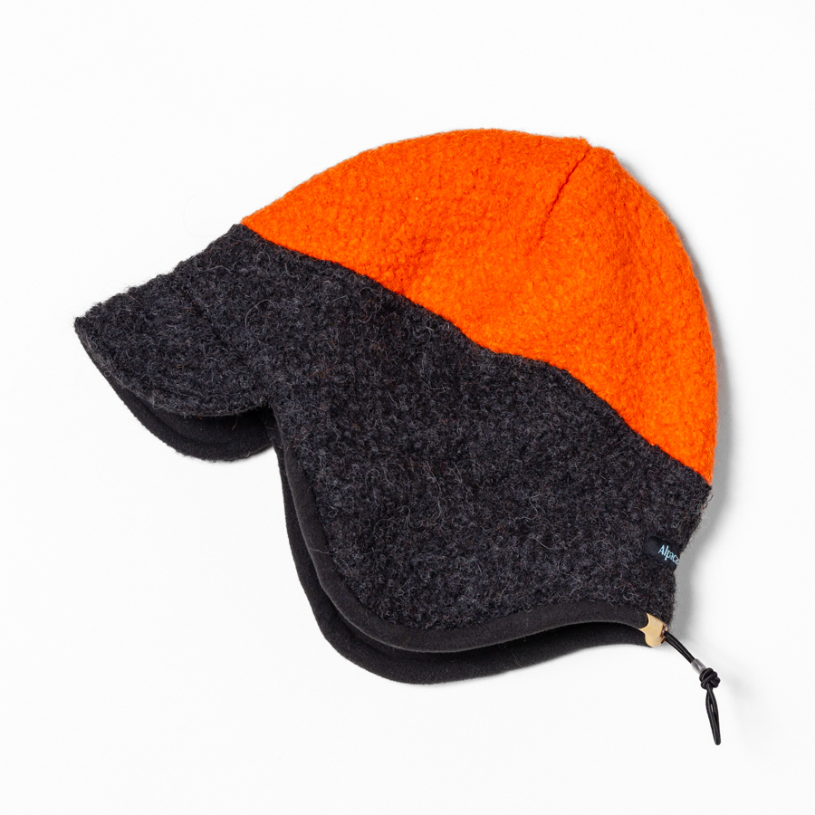 A hunting hat with a dark gray to black gradient on the bottom and bright orange on the top, featuring earflaps and a neck cape.