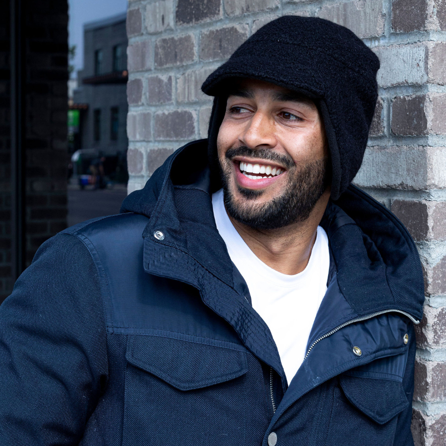 Person smiling outdoors while wearing a black Extreme Warmth alpaca hat with ear coverage, paired with a navy winter jacket. The soft alpaca material and structured design highlight the hat’s warmth and sleek, modern style.