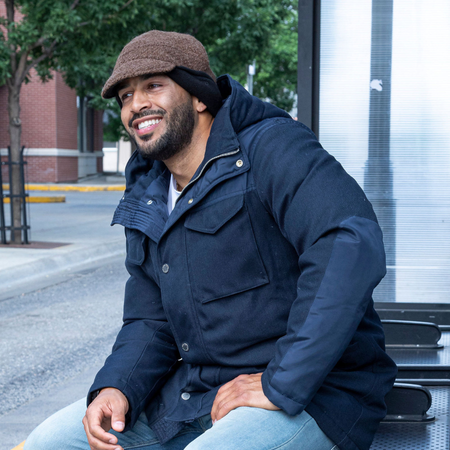 A man in a navy blue jacket wearing a Brown hat with the earflaps rolled up.