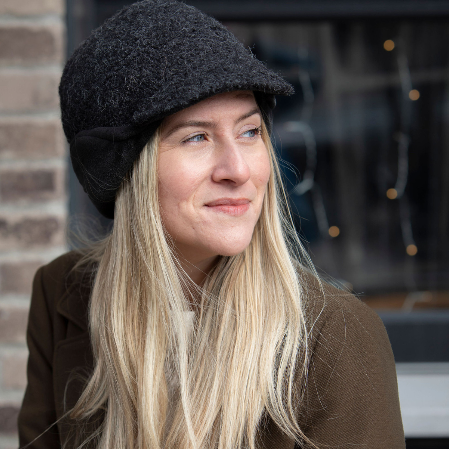 A blonde woman looking to the side wearing a warm Extreme Warmth hat with a brim and earflaps