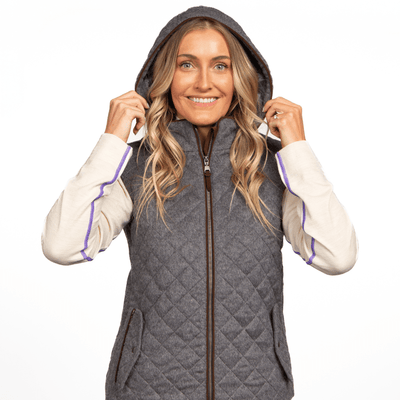 A woman wearing a gray alpaca wool vest with a hood, over a white and brown top, standing against a white background.