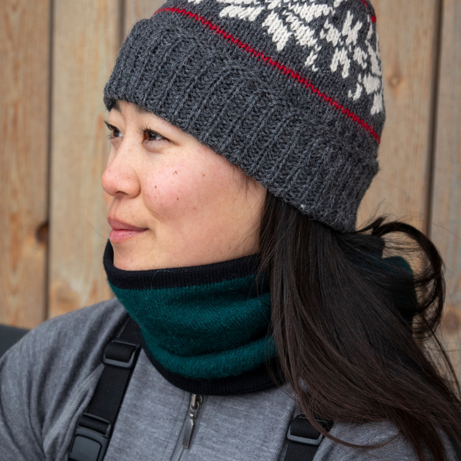 A close up of a woman wearing an Alpacas of Montana lightweight cozy comfortable moisture wicking antimicrobial warm breathable all seasons thin thermal outerwear skiing hiking climbing outdoors hunting fishing rocky mountain neck gaiter made from dark forest green and black alpaca wool.