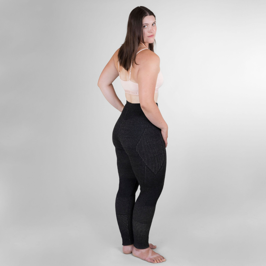 A woman facing sideways standing against a white background. She is wearing a sports bra and a pair of the Alpacas of Montana warm underlayer cozy comfortable thermal moisture wicking long johns winter outerwear heavyweight antimicrobial alpaca wool women&#39;s red and black base layer bottoms for skiing, snowboarding, ice fishing, hunting, camping, arctic, travel