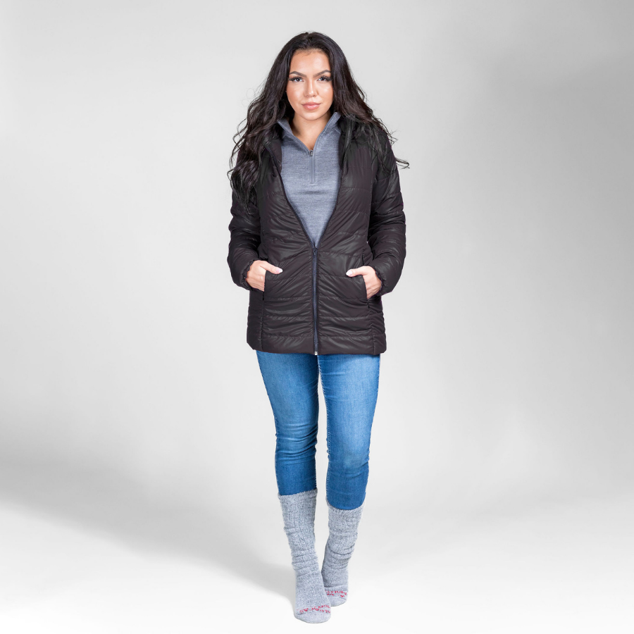 A woman with black hair standing in front of a white background. She is wearing silver gray Alpacas of Montana arctic socks, blue jeans, a gray Alpacas of Montana women&#39;s base layer top, and a black Alpacas of Montana warm top layer insulated cozy comfortable thermal winter outerwear heavyweight alpaca wool lined electric peak parka jacket coat for skiing, snowboarding, ice fishing, hunting, camping, arctic, travel, outdoors