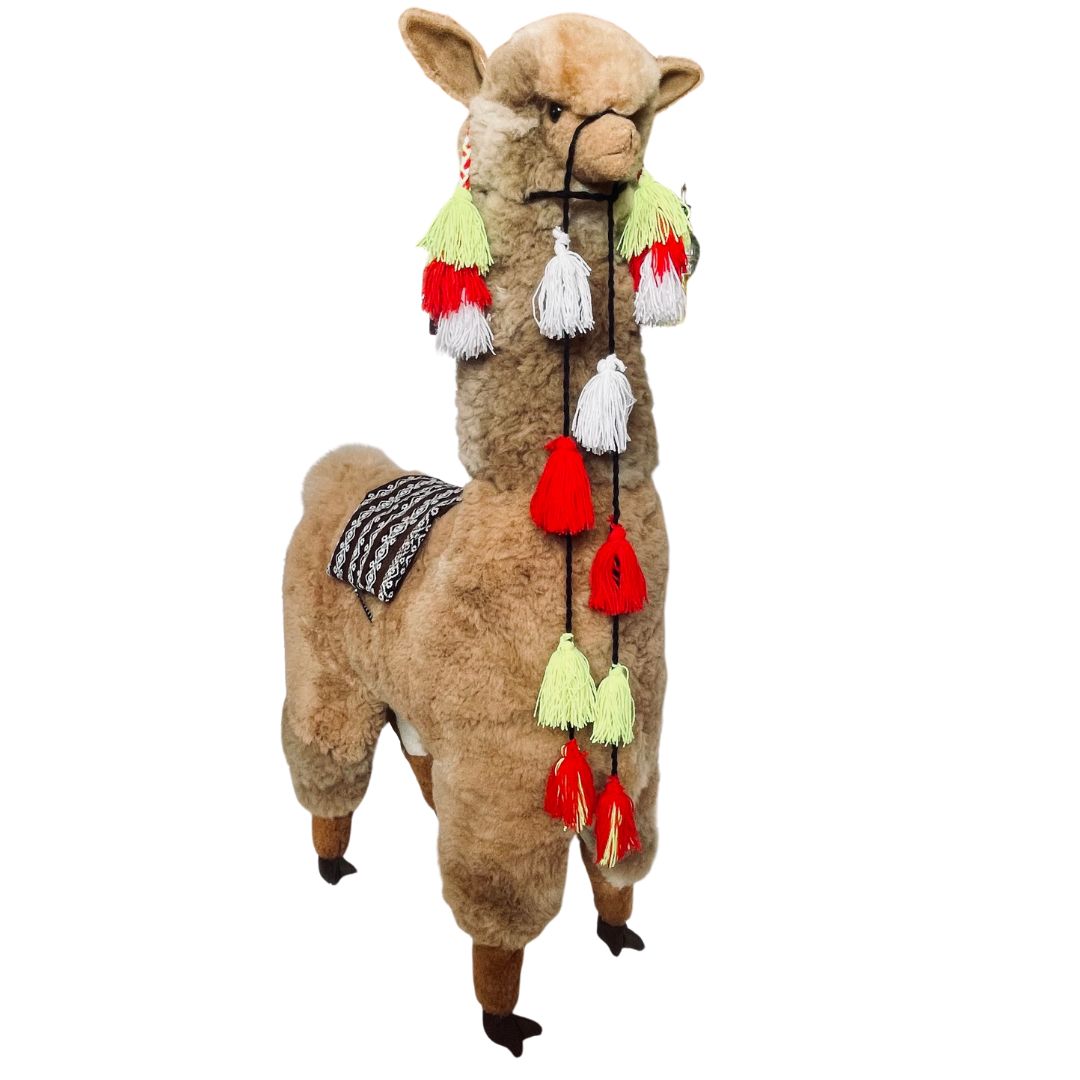 Product photo of a 45 inch tall soft fluffy fawn color alpaca wool plush figurine with red, lime, and white tassels hanging from its halter.
