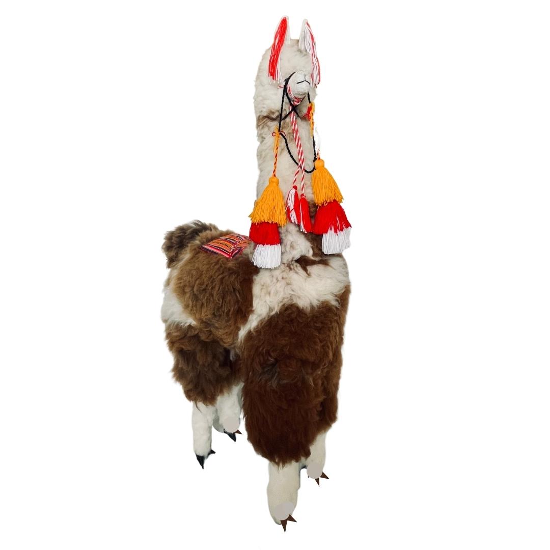 Product photo of a 45 inch tall soft fluffy brown and natural white color alpaca wool plush figurine with red, orange, and white tassels hanging from its halter and ears.