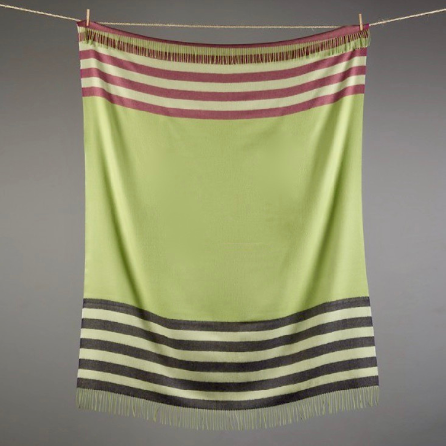 A gray background behind a clothesline with a hanging soft lightweight moisture wicking cozy comfortable lounge accessory interior design fun colorful Alpacas of Montana chartreuse green, maroon, and black alpaca fleece wool throw blanket