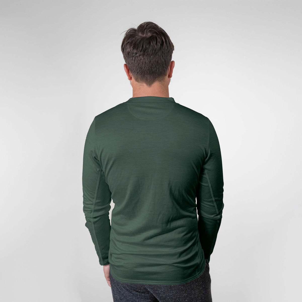 A man facing away from the camera against a white background. He is wearing a forest green Alpacas of Montana lightweight athletic activewear outerwear breathable moisture wicking antimicrobial soft comfortable exercise long alpaca men&#39;s performance tee for running sports exercise work out hiking climbing camping hunting skiing biking