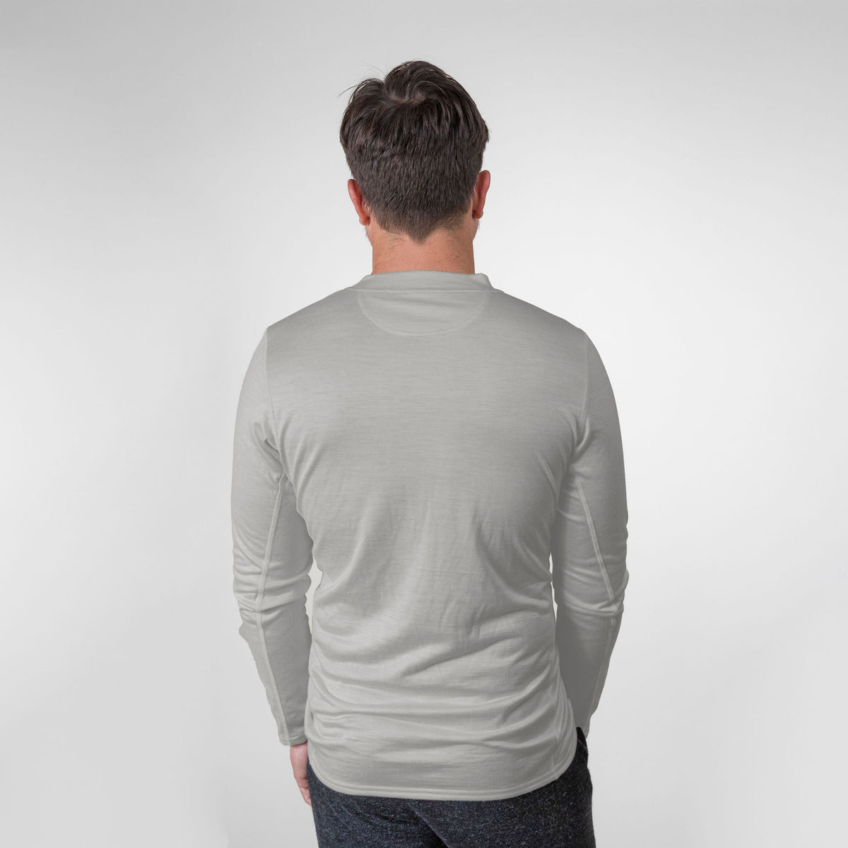 A man standing and facing away from the camera against a white background. He is wearing an Alpacas of Montana lightweight athletic activewear outerwear breathable moisture wicking antimicrobial soft comfortable exercise long sleeve natural white alpaca men&#39;s performance tee for running sports exercise work out hiking climbing camping hunting skiing biking
