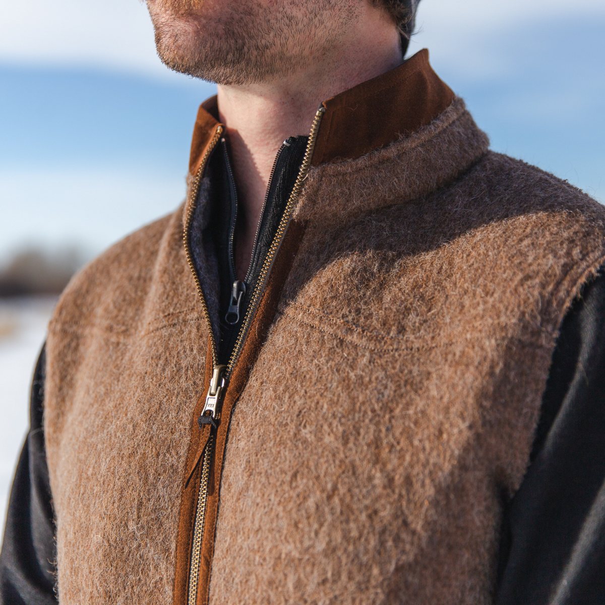 A close up photo of a man wearing a long sleeve back shirt under an Alpacas of Montana camel brown and gray warm soft cozy comfortable neutral moisture wicking men&#39;s fashion stylish luxury zip manly reversible felted alpaca wool vest. 