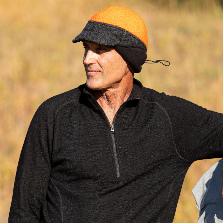 A man standing in bright sunlight wearing an Alpacas of Montana mid-layer long sleeve top and a gray and orange extremely warm cozy soft windproof comfortable moisture wicking thermal alpaca fleece wool windstopper winter hat for hiking, skiing, hunting, fishing, outdoors.