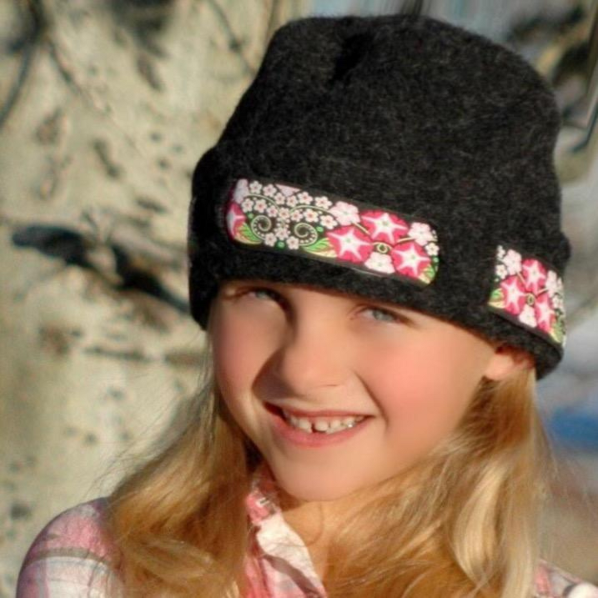 A blonde little girl wearing a soft cozy cute warm winter thermal moisture wicking felted dark gray alpaca wool beanie hat with a black, white, and pink floral ribbon for kids children