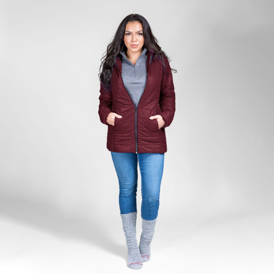 A woman with black hair standing in front of a white background. She is wearing silver gray Alpacas of Montana arctic socks, blue jeans, a gray Alpacas of Montana women&#39;s base layer top, and a dark cherry cranberry red Alpacas of Montana warm top layer insulated cozy comfortable thermal winter outerwear heavyweight alpaca wool lined electric peak parka jacket coat for skiing, snowboarding, ice fishing, hunting, camping, arctic, travel, outdoors