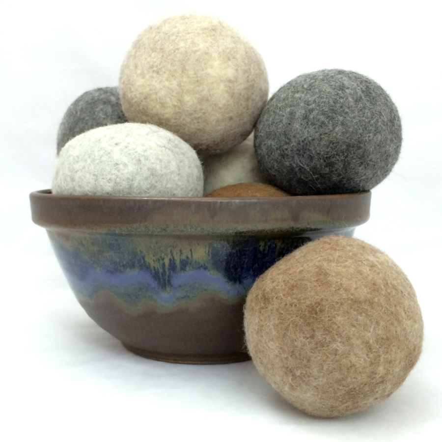 A clay bowl filled with alpaca wool dryer balls of various muted, natural colors.