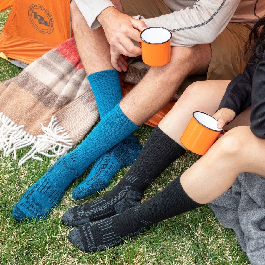 Two people sitting in the doorway of a tent wearing Alpacas of Montana activewear outdoors athletic adventure hiking socks in blue and black.
