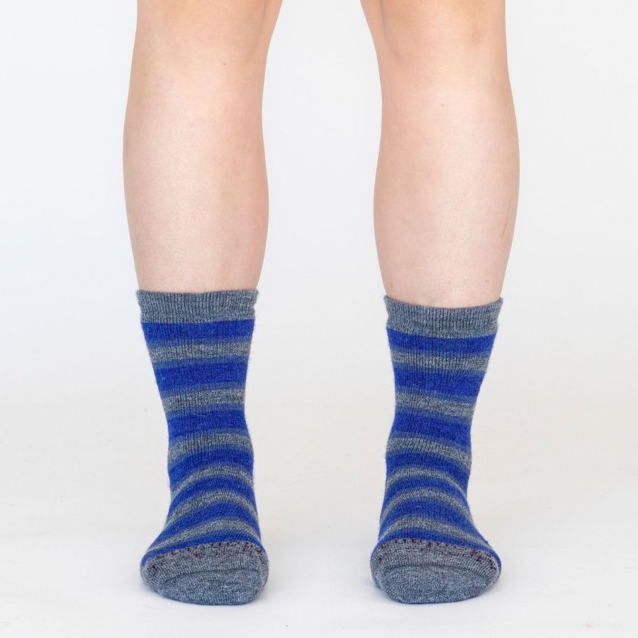 A knees-down photo of a person standing in front of a white background wearing a pair of the soft cozy comfortable moisture wicking lounge and active everyday medium gray and blue striped basecamp socks.