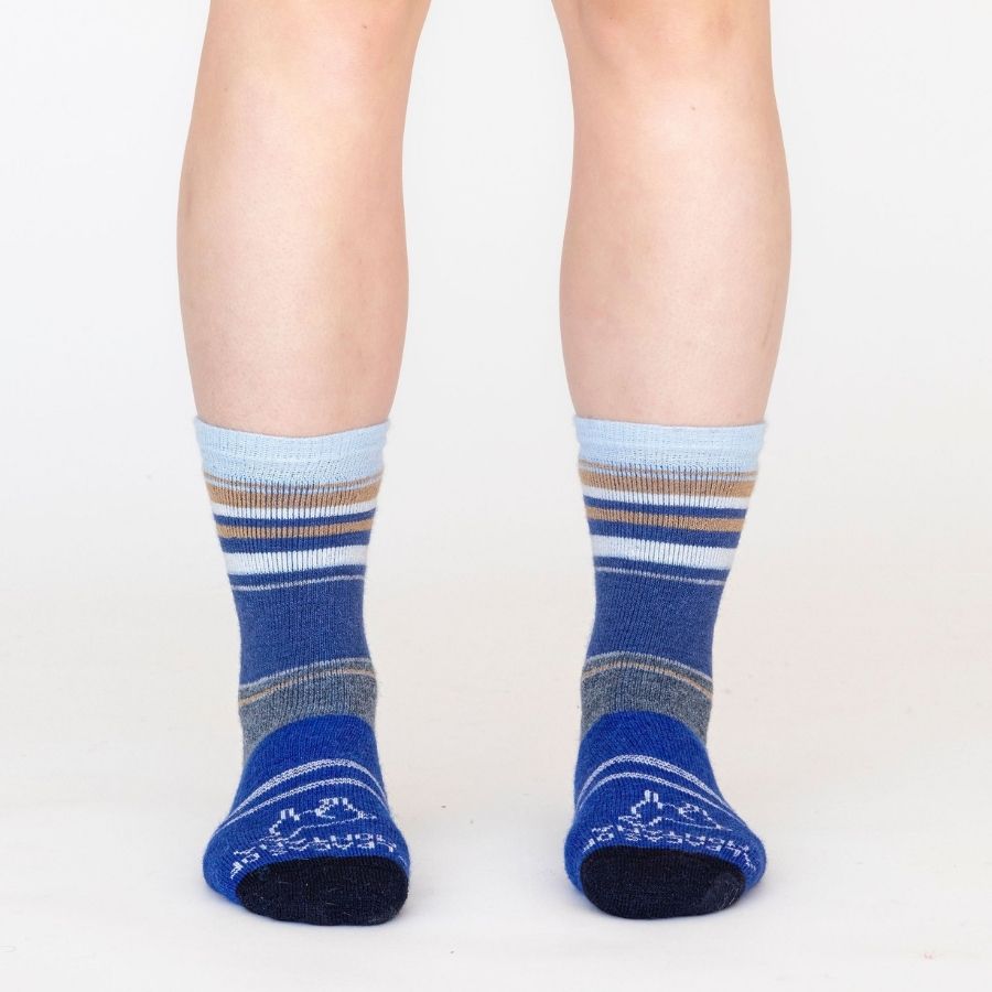 A knees-down photo of a person standing in front of a white background wearing a pair of the soft cozy comfortable moisture wicking lounge and active everyday bright blue, navy, cobalt, black, sky blue, gold, and natural white striped basecamp socks.
