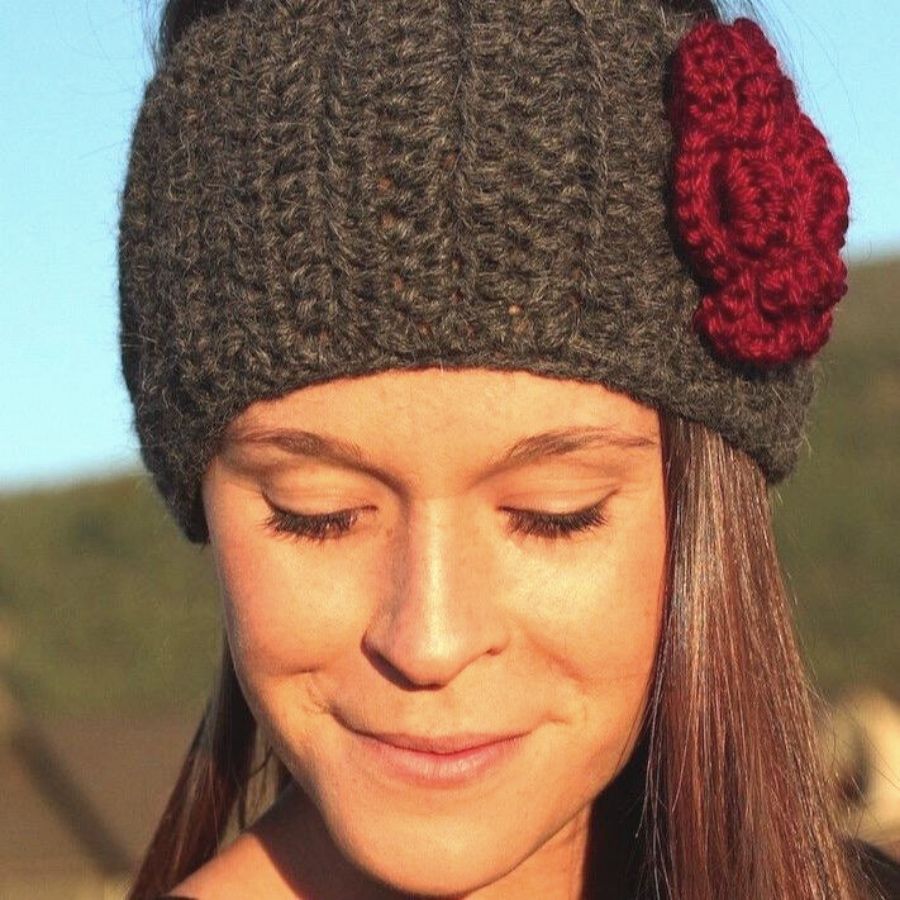 A smiling brown haired woman looking down wearing a soft cute stylish fashion cozy comfortable warm winter headband and flower accessory handmade knit crochet in Montana from brown and scarlet red alpaca yarn