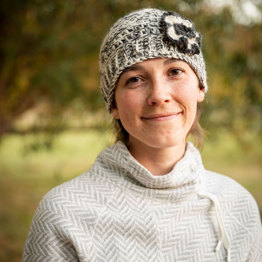 woman smiling wearing gray white and black hand knit alpaca wool hat with flower