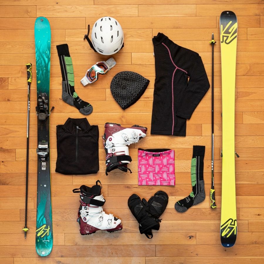 flat lay picture of skis, ski socks, boots, a helmet, goggle, gator, mittens and fleece lined hat
