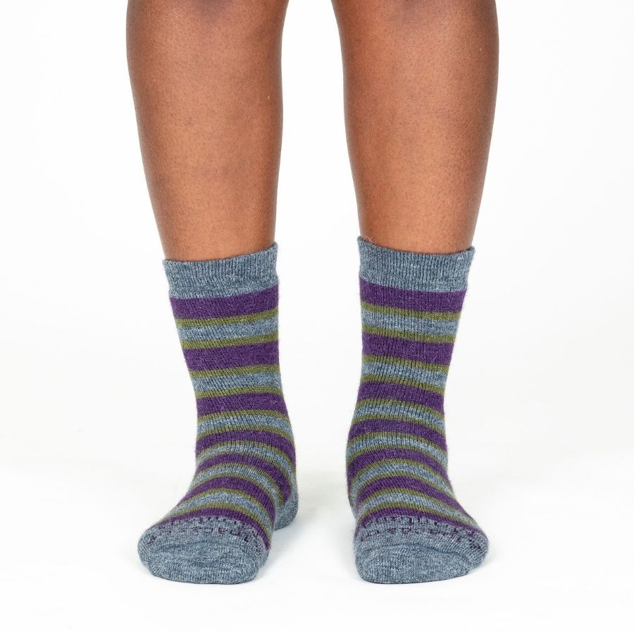 A knees-down photo of a person standing in front of a white background wearing a pair of the soft cozy comfortable moisture wicking lounge and active everyday medium gray, green, and purple striped basecamp socks.
