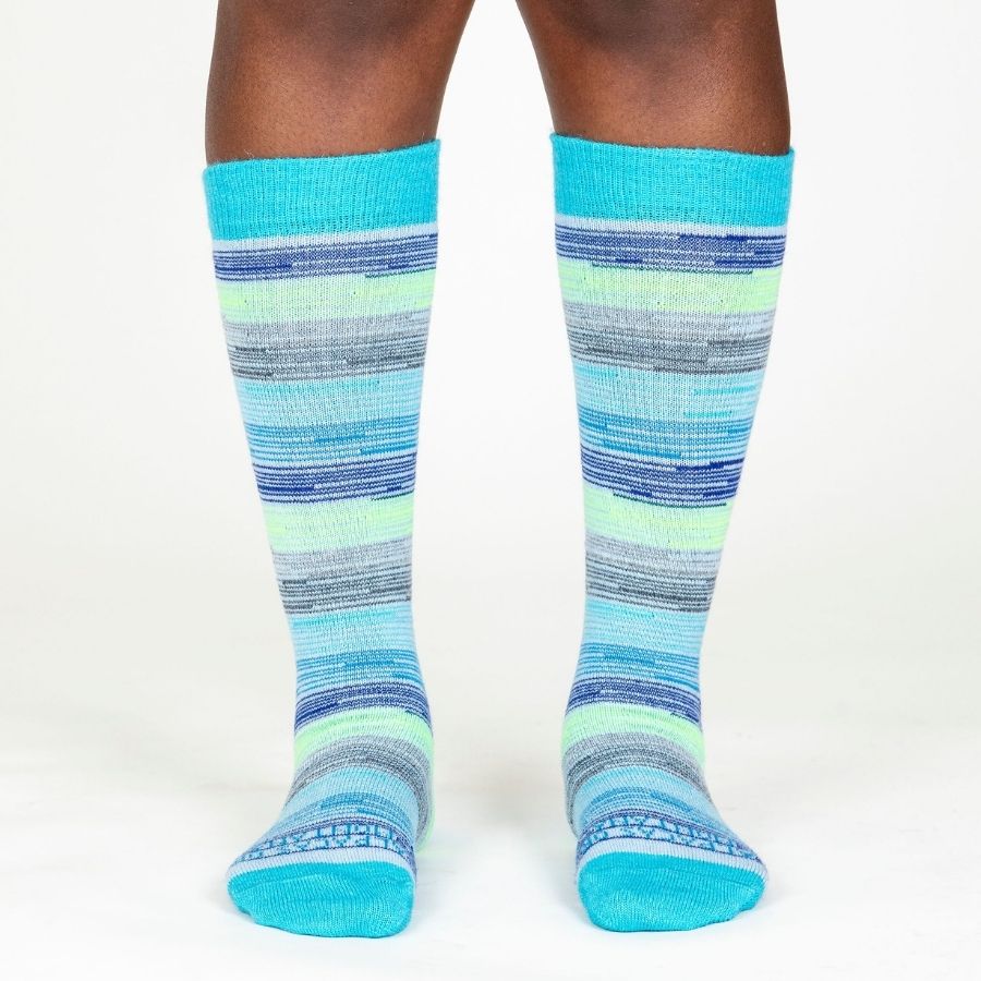 A person&#39;s lower legs with a white background wearing Alpacas of Montana colorful navy, cobalt, sky blue, lime green, gray, and black casual lounge fashion comfortable soft cozy everyday moisture wicking alpaca wool striped socks.