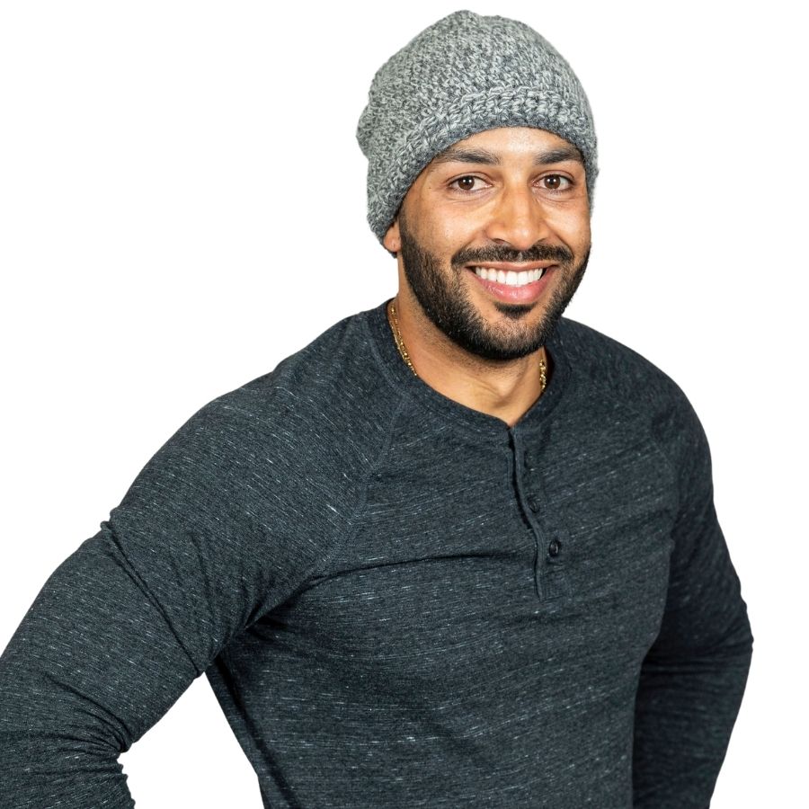 A man with a black beard standing against a white background. He is wearing a dark gray long sleeve shirt and an Alpacas of Montana soft cozy comfortable stylish thermal fashionable moisture wicking antimicrobial knitted crochet mountaineer skullcap beanie hat handmade in Montana from light gray and multi-gray alpaca wool and bamboo yarn.
