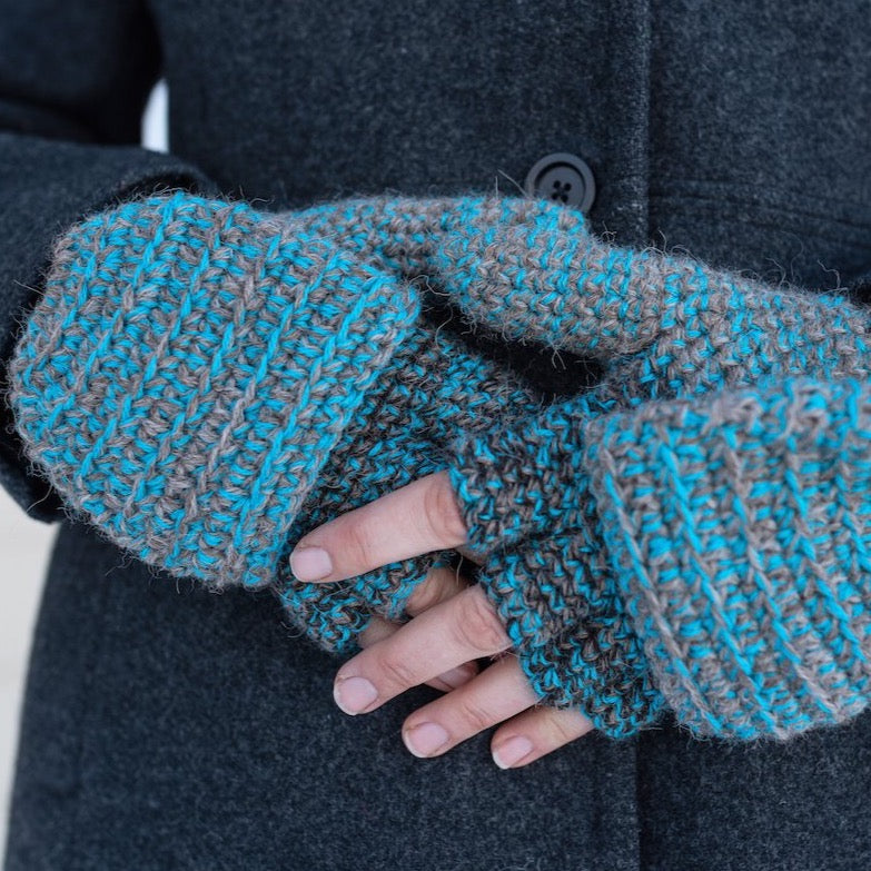 A close up photo of a pair of hands wearing soft warm winter stylish cozy comfortable fashionable moisture wicking knitted crochet heavyweight flip top gloves mittens handmade in Montana from gray, black, and bright teal blue alpaca wool yarn.