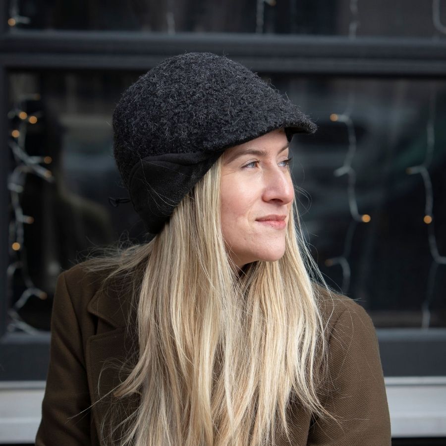 A blonde woman smiling and looking sideways wearing a dark gray extremely warm cozy soft windproof comfortable moisture wicking thermal winter alpaca fleece wool city commuter hat.
