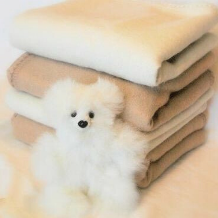 four soft alpaca wool baby blankets stacked on each other with a white alpaca wool teddy bear in front of them