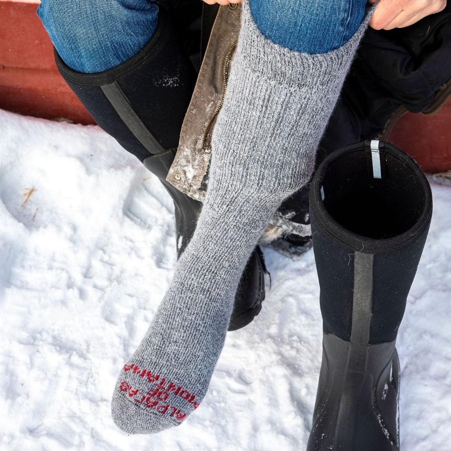 A close up photo of someone pulling up a pair of soft extreme warmth cozy comfortable warm winter arctic thermal moisture wicking alpaca wool knee-high socks.