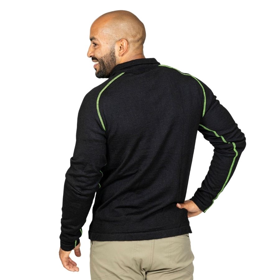 A smiling bald man with a black beard standing facing away from the camera with one hand on his hip in front of a white background. He is wearing khaki pants and a black with lime green stitching Alpacas of Montana warm thermal soft cozy comfortable activewear outerwear athletic moisture wicking antimicrobial men&#39;s fashion stylish luxury mid-layer quarter-zip alpaca wool long sleeve pullover top for outdoors camping climbing hiking skiing hunting fishing running winter.