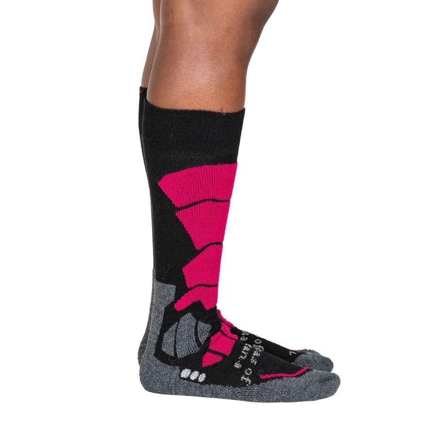 A person&#39;s lower legs standing sideways with a white background wearing fuchsia pink, gray, and black Alpacas of Montana cozy comfortable soft warm thermal winter freezing temperatures antimicrobial moisture wicking alpaca wool ski and snowboard socks for snowshoeing, skiing, snowboarding, ice fishing, outdoors.