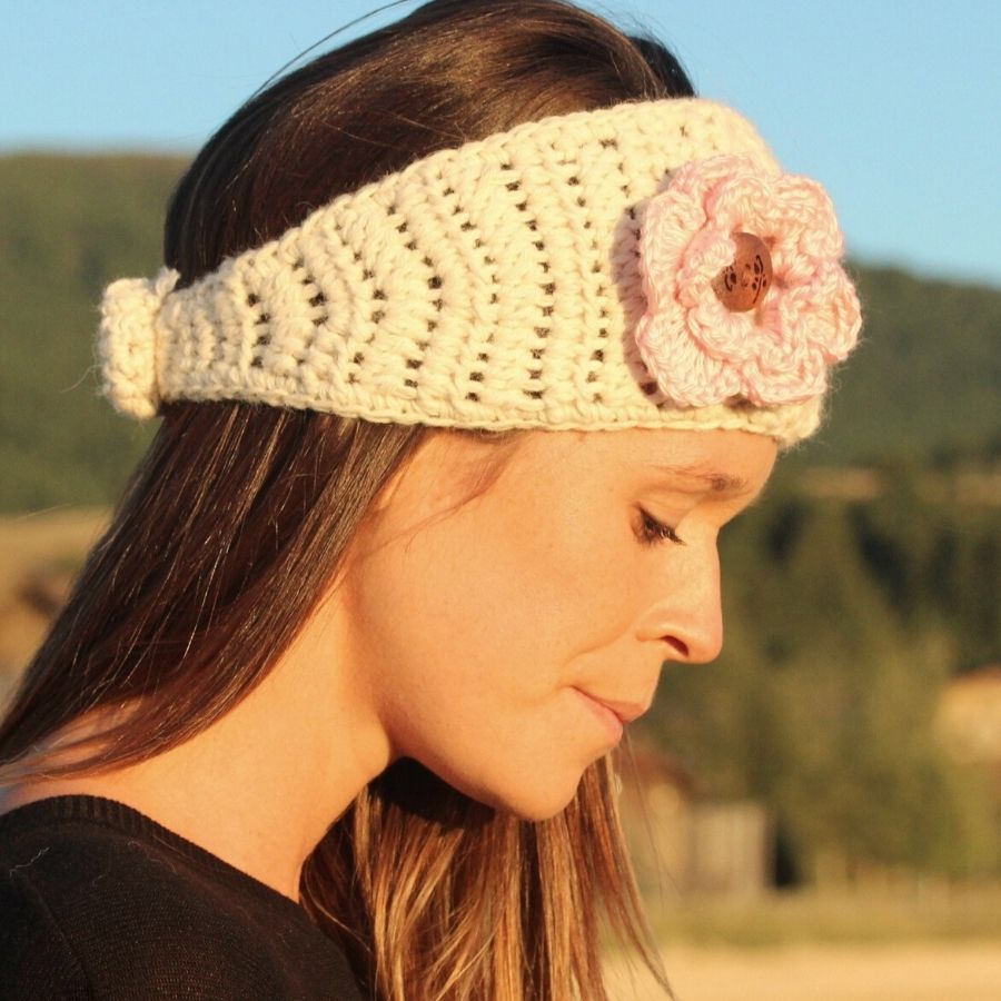 A brown haired woman looking down wearing soft cute stylish fashion cozy comfortable warm winter headband and flower accessory handmade knit crochet in Montana from natural white and light pink alpaca yarn