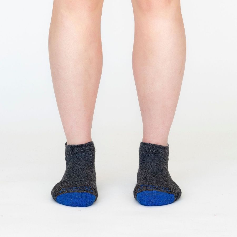 A person&#39;s lower legs in front of a white background wearing Alpacas of Montana soft comfortable breathable athletic outerwear activewear moisture wicking antimicrobial gray and royal blue swift wicking running sock for running, sports, hiking, exercise.